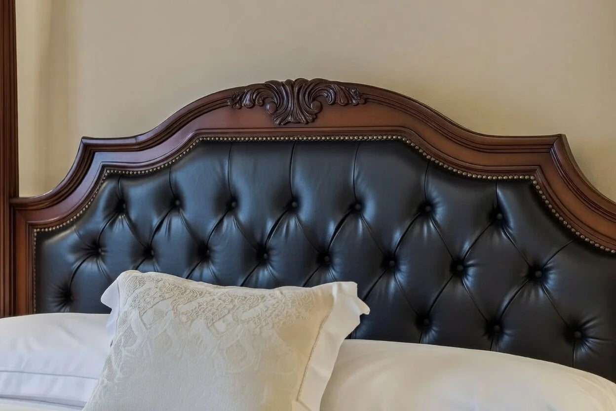 Close-up of a hand-carved solid wood headboard featuring intricate regency-style scrollwork and premium black tufted leather upholstery with nailhead trim.