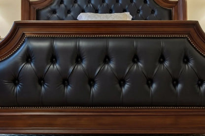 Detail of a classic four-poster bed footboard with deep button-tufting in black leather and an antique-finished solid wood frame.