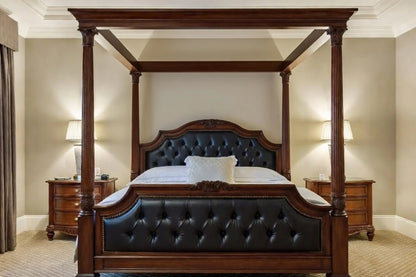 Luxury canopy bed in traditional regency style, handcrafted from solid teak wood with a black button-tufted leather headboard and footboard.