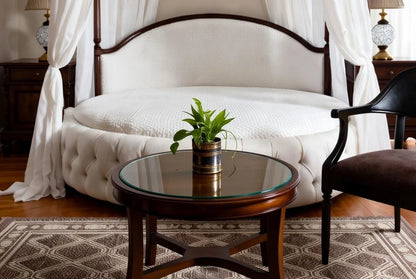 Close-up detail of the white button-tufted round bed base with a small glass-top coffee table in the foreground.