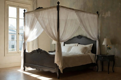 Four-poster bed with white canopy and bedding in a room with large windows.