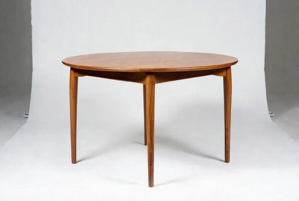 Classic mid-century round walnut dining table with smooth oval top and four splayed tapered legs, Danish modern minimalist furniture