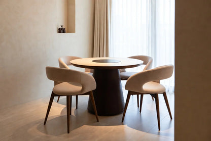 Modern round walnut dining table with flush dark Lazy Susan center, surrounded by 4 curved beige upholstered armchairs, minimalist luxury dining set
