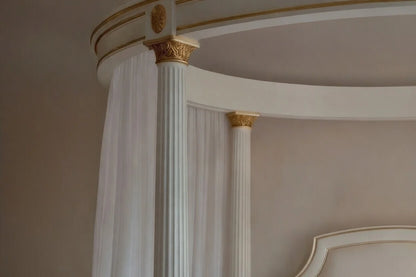 Detail of the fluted pillars and hand-carved top rail of a bespoke circular canopy bed in white and gold.