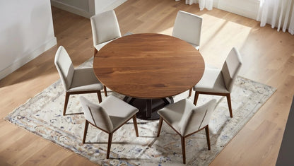 Scandinavian round walnut dining table with modern black X-shaped base, surrounded by six beige upholstered chairs in a bright contemporary dining room