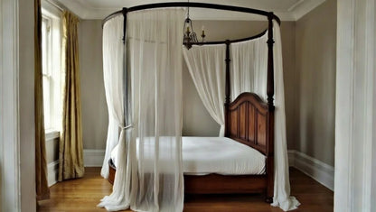Side view of a dark walnut four-poster bed with sheer white drapes hanging from a round canopy ring.